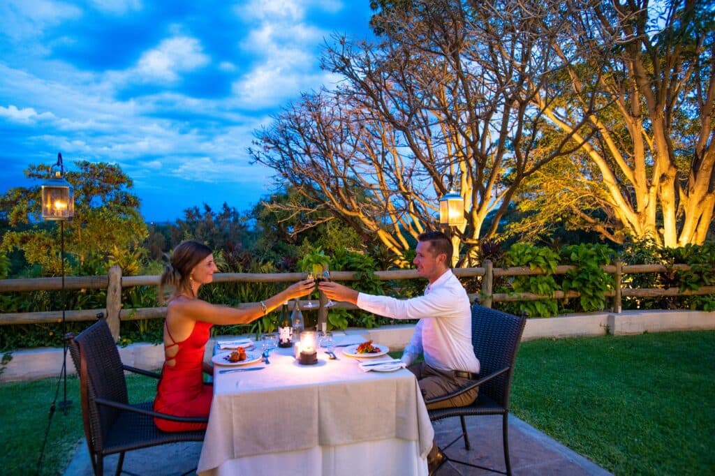 A couple toasts with wine glasses at an outdoor dinner table at dusk