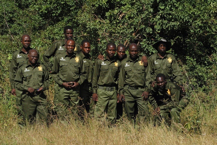 A group of ten rangers in green uniforms posing outdoors against a backdrop of dense foliage