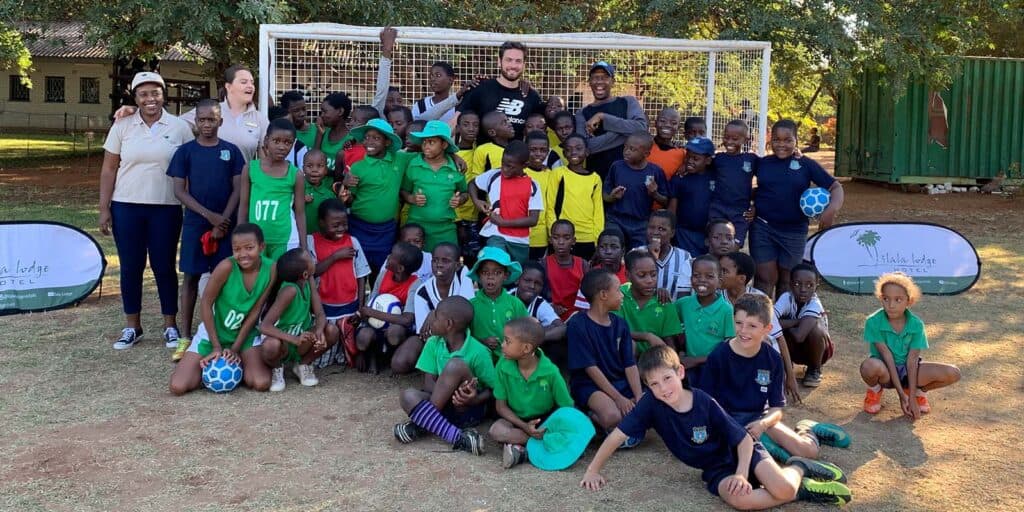 Group of children and adults posing together on a grassy field in front of a soccer goal