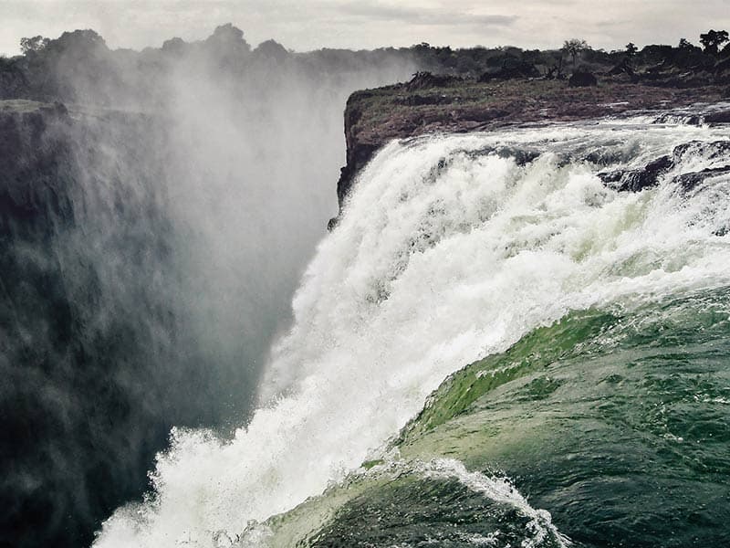 Rushing water plunges over the edge of a vast waterfall, creating a heavy mist that fills the deep canyon