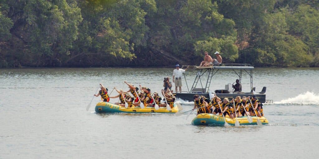 Two yellow rafts with teams of people paddling on a river, accompanied by a motorized safety boat