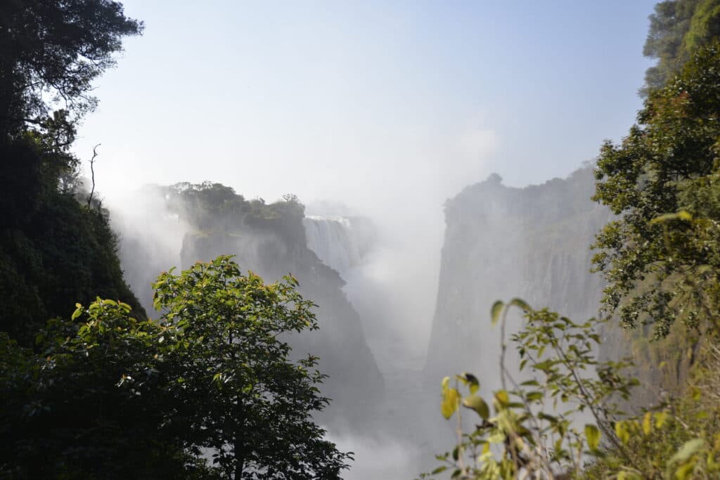 A large waterfall cascading into a deep gorge, partially obscured by heavy mist and framed by lush green trees