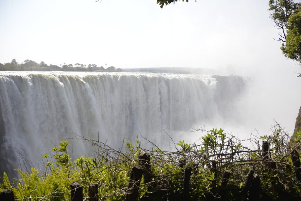 A wide curtain of water plunges over a massive cliff, creating heavy mist that partially obscures the right side